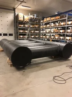 Sorte rørdeler lagt på pall i lagerhall.