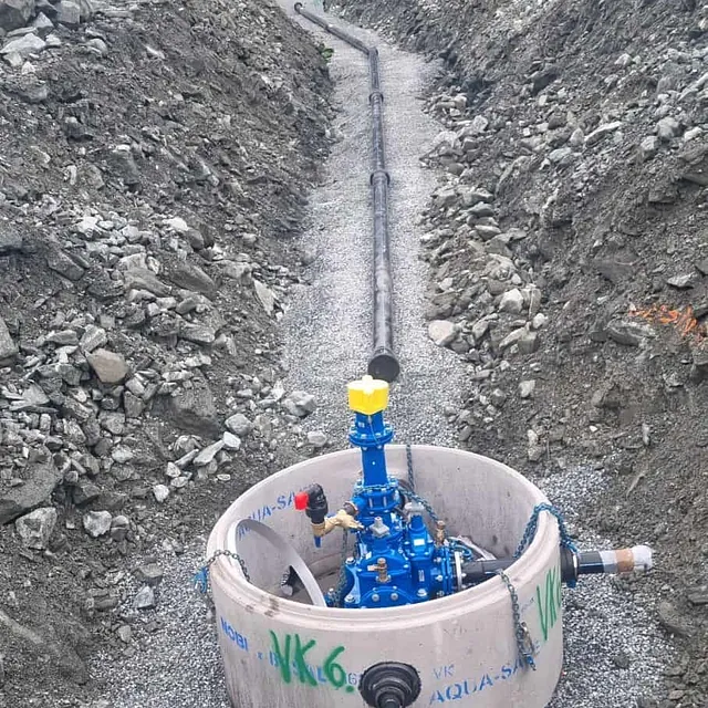 Betongkum med blå ventiler i grøft, rør lagt gjennom steinmasser.